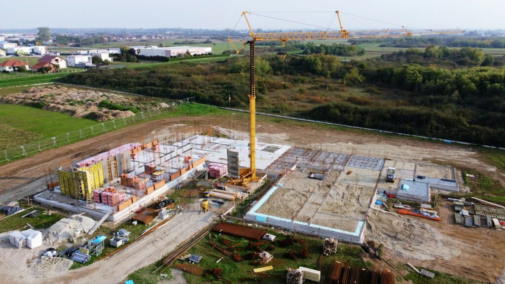 Aerial drone photo of a construction site with a tower crane, foundations and staged materials